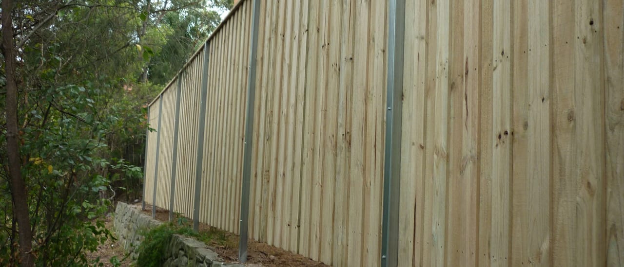 Lap and cap treated pine timber fence with a timber capping rail along the top, built above an existing sandstone retaining wall in Sydney