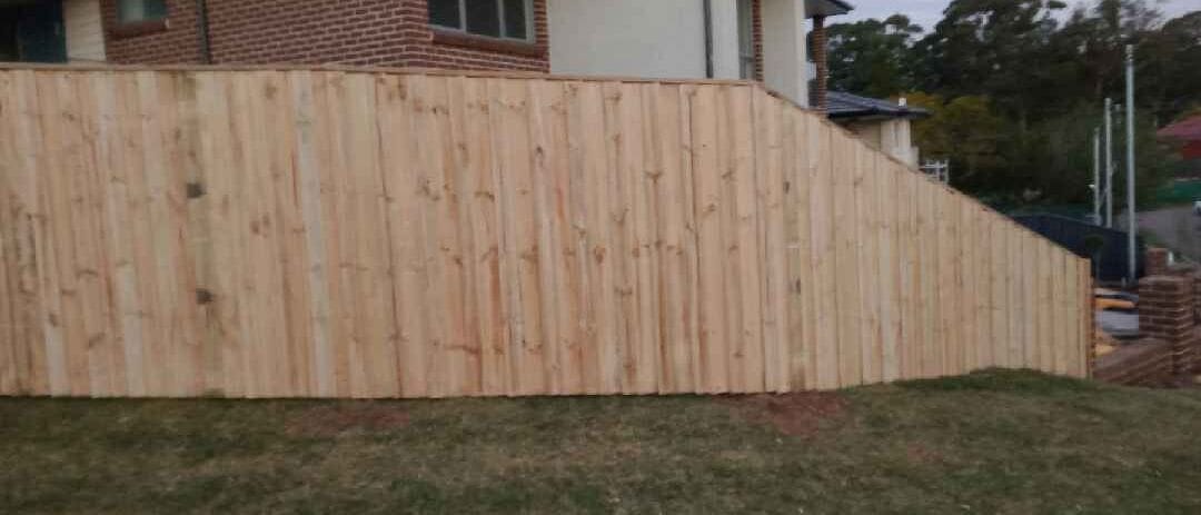 Treated pine timber fence stepped down a sloping boundary behind a brick home in Sydney