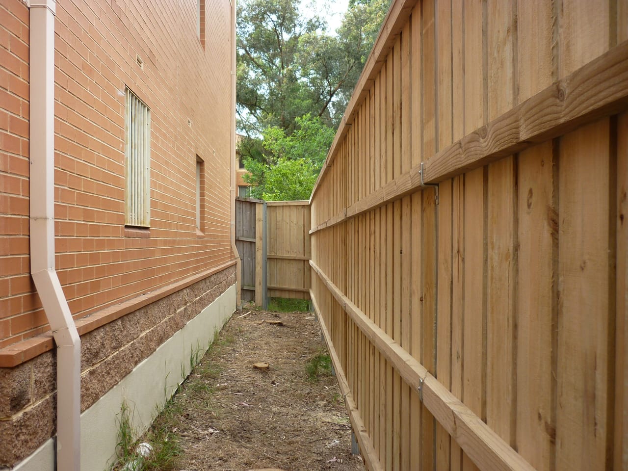 Tall treated pine timber fence installed along a narrow side boundary between a brick house and the neighbouring property